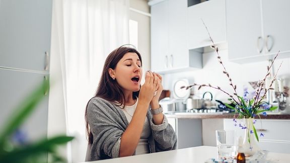 Woman sneezing from allergies about to take medicine from allergist